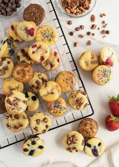 muffins and other treats are on a cooling rack next to strawberries, nuts, and chocolate chips