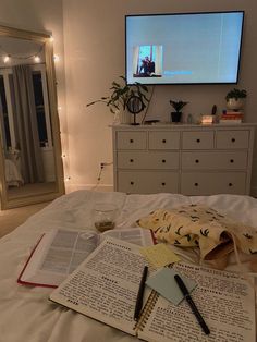 an open book on a bed in front of a flat screen tv with writing and pens