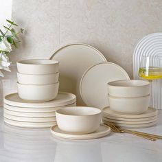 white dishes and cups are arranged on a countertop next to a vase with flowers