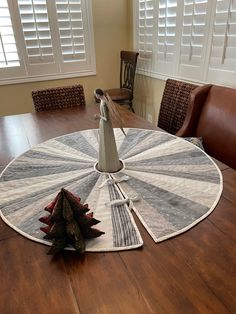 a wooden table topped with a white and gray quilted centerpiece on top of a wooden dining room table