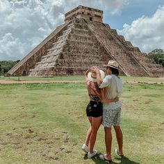 two people are standing in front of an ancient pyramid with a hat on their head