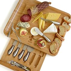 a cutting board with cheese, meats and bread on it next to utensils