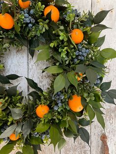 an orange and blue berry wreath hangs on a white wooden door with greenery around it