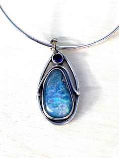 I did the silversmith work on this amazing pendant. It has an amazing opal at 54 carats.  I set this in a unique silversmith style I learned recently from an a wonderful silversmith teacher.  The top stone is a man-made faceted blue sapphire.  It can be changed up as you desire.  If you want the bail changed - I can do this.  I made the bail from a 20 gauge silver piece of wire.   You can request a silver extension length chain or a pre-fashioned silver piece to fit closely around the neck.  Is organic and beautiful.  I have to admit I was stunned at how beautiful it came out. Polished Opal Pendant Jewelry, Opal Large Pendant Jewelry, Artisan Silver Opal Necklace, Blue Opal Round Pendant Jewelry, Sapphire Jewelry With Silver Cabochon, Blue Opal Pendant Jewelry, Silver Sapphire Jewelry With Cabochon, Elegant Opal Jewelry With Large Pendant, Artisan Silver Opal Jewelry