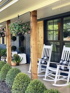 two white rocking chairs sitting on top of a porch next to bushes and potted plants