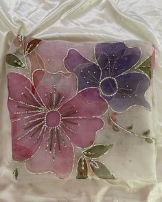 a pink and purple flower is on a white sheet with pearls in the center, surrounded by green leaves