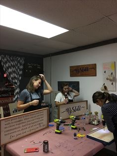 three girls are standing around a table with items on it and one girl is holding her head up