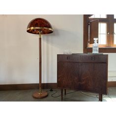 a lamp sitting on top of a wooden cabinet next to a wine glass filled bottle