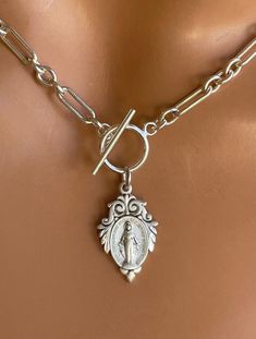 "This is a stunning thick, solid 925 sterling silver choker necklace with a unique Virgin Mary medallion that hangs from toggle clasp in front. This gorgeous Mother Mary charm measures 22x14mm and has the Miraculous Mary stamp with cross heart and stars on backside.. Made here is the USA by skilled silversmiths this pendant is absolutely incredible. This lovey sterling silver chunky chain links measure 8x4mm and 4mm, 3-1 pattern. Model is wearing a 15\" choker length. Comes in a gift box, ready Silver Sterling Silver Chain Necklace With Charms, Handmade Sterling Silver Chain Choker, Silver Engraved Lariat Jewelry, Sterling Silver Choker With Lobster Clasp, Silver Link Necklace With Charms, Silver Link Necklaces With Charms, Silver Link Jewelry With Charms, Elegant Silver Toggle Necklace With Oval Link, Elegant Silver Toggle Necklace With Round Pendant