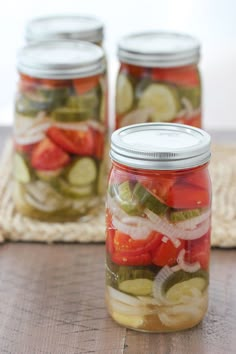 three jars filled with pickles and cucumbers on top of a wooden table