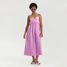 a woman wearing a purple dress and sunglasses standing in front of a white background with her hands on her hips