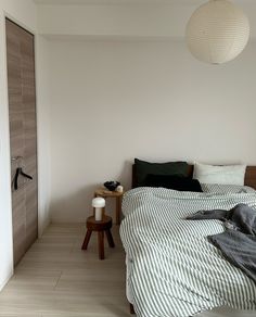 an unmade bed in a bedroom with white walls and wood flooring next to a wooden side table