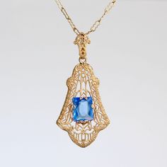 "Circa 1920, a lovely filigree lavaliere necklace crafted in 10k yellow gold set with a glittering cornflower-blue crystal gem. There's an amazing degree of intricacy to the airy design of the pendant with its graceful zig-zags and delicate milgraining, the glowing color of the metal perfectly complemented by the cool sparkle of the stone. Measuring approximately 1 1/2\" north to south including the decorative bail, and 3/4\" east to west. Hung on a fine 14k gold 15 1/8\" vintage crimp link chai Blue Pendant Jewelry, Custom Gift Boxes, Blue Pendant, Necklace Craft, Yellow Gold Setting, Filigree Design, Blue Gems, Blue Jewelry, Cornflower Blue