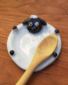 a ceramic plate with a wooden spoon on it and a black sheep face painted on the top