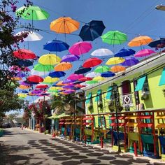 many colorful umbrellas are hanging from the wires above tables and chairs on an empty street