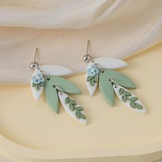 two pairs of earrings with green leaves and flowers on them