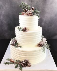 a three tiered white cake with pine cones on top