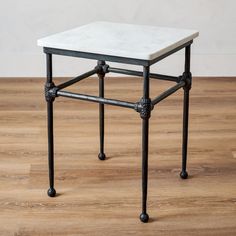 a white marble top side table with black metal legs on a wood floor in an empty room