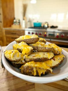 baked potatoes with cheese and meat on a white plate sitting on a wooden table in front of an oven