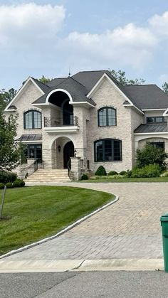 a large white brick house with green trash cans in front of it and grass around the driveway