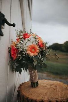 an orange and white bouquet sitting on top of a tree stump next to a window