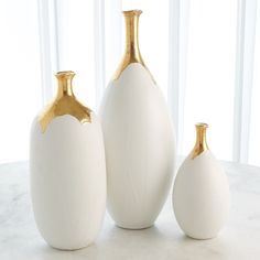 three white and gold vases sitting on top of a marble table next to each other