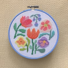 a cross - stitch pattern with flowers on it is hanging from a hook in front of a beige wall