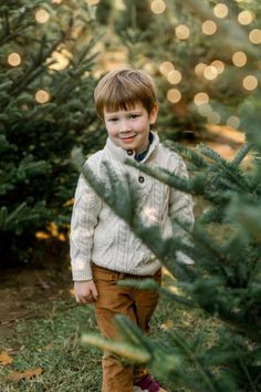 a young boy standing in front of a christmas tree with lights on the trees behind him