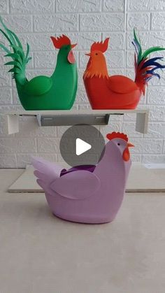 three colorful plastic chickens sitting on top of a white shelf in front of a brick wall