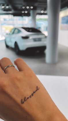 a person's hand with a small tattoo on their left wrist, next to a parked car