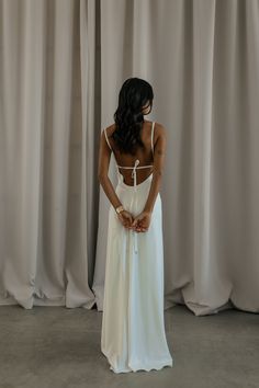 a woman wearing a white dress standing in front of curtains with her back to the camera