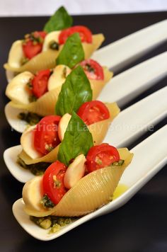 four pasta shells with tomatoes and spinach on white serving utensils, ready to be served