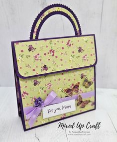 a handmade purse with flowers and butterflies on the front, purple ribbon around the handle