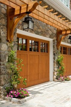 two wooden garage doors are open on the side of a stone building with flowers in front