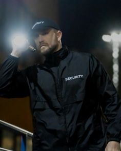 a man in a black jacket and hat holding a cell phone to his ear while standing outside at night