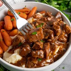 a bowl filled with meat and potatoes covered in gravy next to carrots