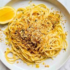 pasta with parmesan cheese and lemon on a white plate next to a slice of lemon