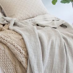 a bed covered in blankets and pillows next to a plant