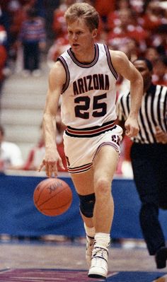 a young man dribbling a basketball during a game with an official on the sidelines