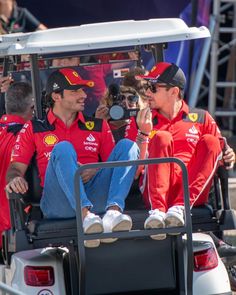 two men in red shirts and jeans sitting on a golf cart talking to each other