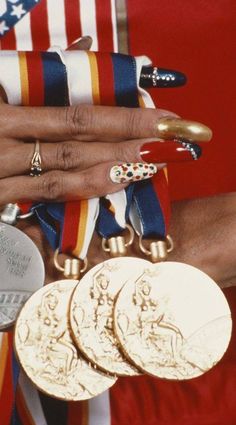 a woman's hands with gold and silver rings on her wrist, holding three medals