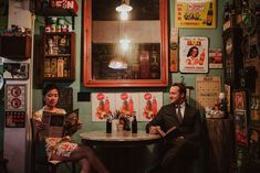 a man and woman sitting at a table in a room with posters on the wall