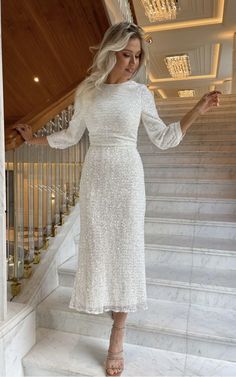 a woman in a white dress is standing on the stairs and holding a glass of wine