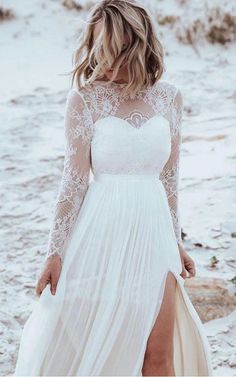 a woman standing on top of a sandy beach wearing a white dress with sheer sleeves