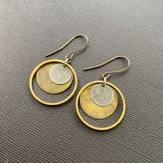 Attract the energy of wellbeing in these modern art mixed metal circle in circle earrings you'll want to wear everyday. These dainty geometric earrings make a perfect Christmas, birthday, graduation or self care gift, or for anyone who appreciates simple, casual elegance. These modern boho earrings feature raw brass hoops, a patina brass disc and a smaller silver-toned disc, with antique brass French earring wires. Handmade by Native American artist/designer Loren Lavine in her California studio, these earrings are infused with healing energies. 🪶 MATERIALS/DIMENSIONS >  Earring measures approximately 1" in length x 1" across. >  Brass, rubber earring backs 🪶 STONE/ELEMENT ENERGY >  BRASS is the metal that brings out natural good and inner truth. >  CIRCLES represent wholeness and eterni Boho Wear, Metal Circle, Art Earrings, Earring Wires, Native American Artists, Brass Hoops, Geometric Earrings, Circle Earrings, Mixed Metals