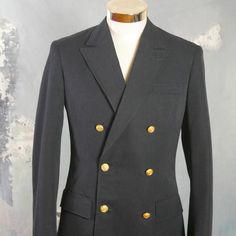 This 1960s German vintage double-breasted naval officer's jacket has peak lapels and padded shoulders, and closes in the front with two gold anchor buttons (six in total show on the front). The handsome blazer has three pockets on the front, and the left chest pocket has small pinholes where a patch was removed. The jacket is lined in a navy blue satin viscose fabric, and has three inner pockets.Brand label: Kleiverfabrik Knab (Germany)Size: 36 US/UKMaterial: 55% polyester, 45% woolCondition: Ex Formal Gold Outerwear With Double-breasted Button Fastening, Fitted Gold Double-breasted Blazer, Gold Double-breasted Blazer With Double Button Closure, Gold Double-breasted Blazer, Gold Fitted Double-breasted Blazer, Fitted Double-breasted Blazer With Gold Buttons, Gold Double-breasted Blazer With Buttons, Classic Outerwear With Gold Buttons And Suit Collar, Classic Double-breasted Blazer With Gold Buttons