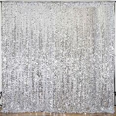 a white curtain with silver sequins hanging from it's side in front of a wooden floor