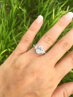 a woman's hand with an engagement ring on top of her finger in the grass