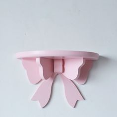 a pink shelf with two bows on it's top, against a white wall