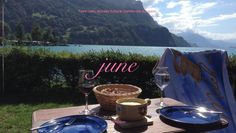 a table with plates and glasses on top of it next to the water in front of mountains